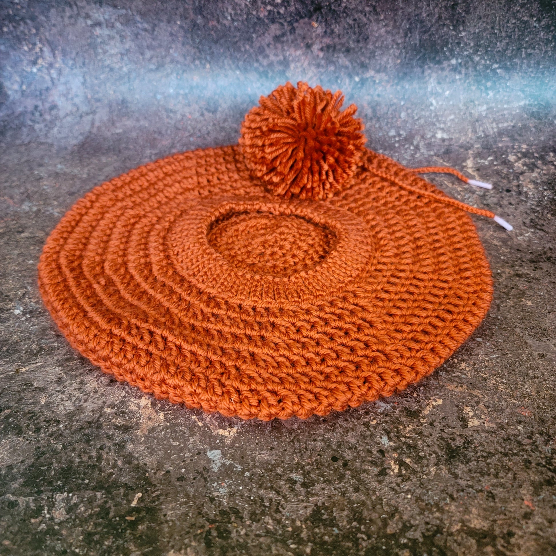 Rusty orange crocheted beret with pom-pom on side, flat lay.