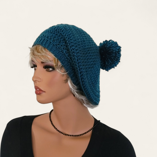 Teal crocheted beret with pom-pom on mannequin.