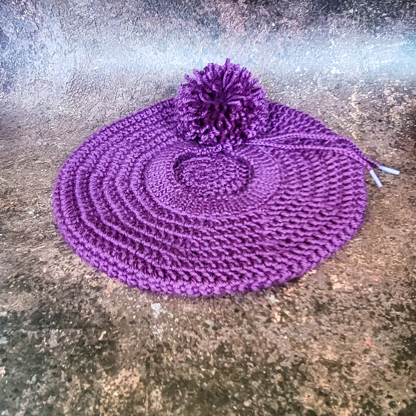 Purple crocheted beret with pom-pom on side, flat lay.