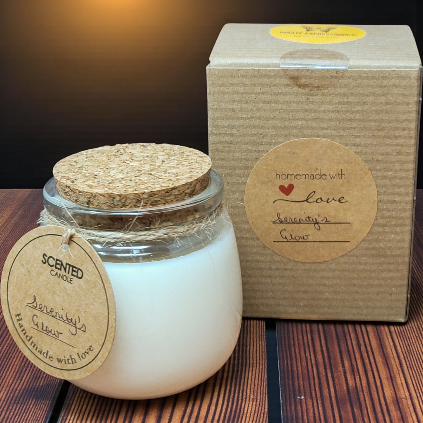 Scented candle in a glass jar with a cork lid next to its cardboard box on a wooden surface.