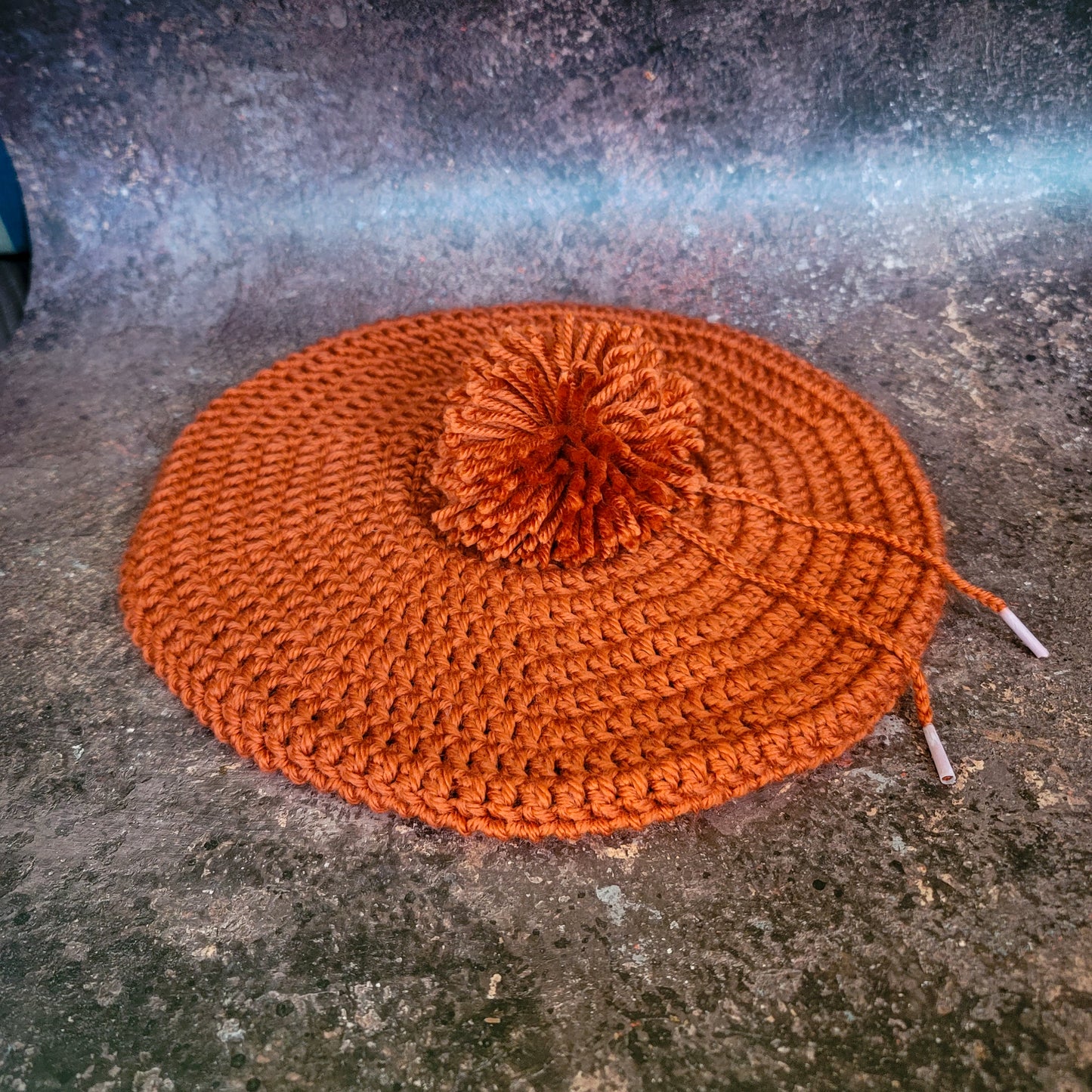Rusty orange crocheted beret with pom-pom, flat lay.