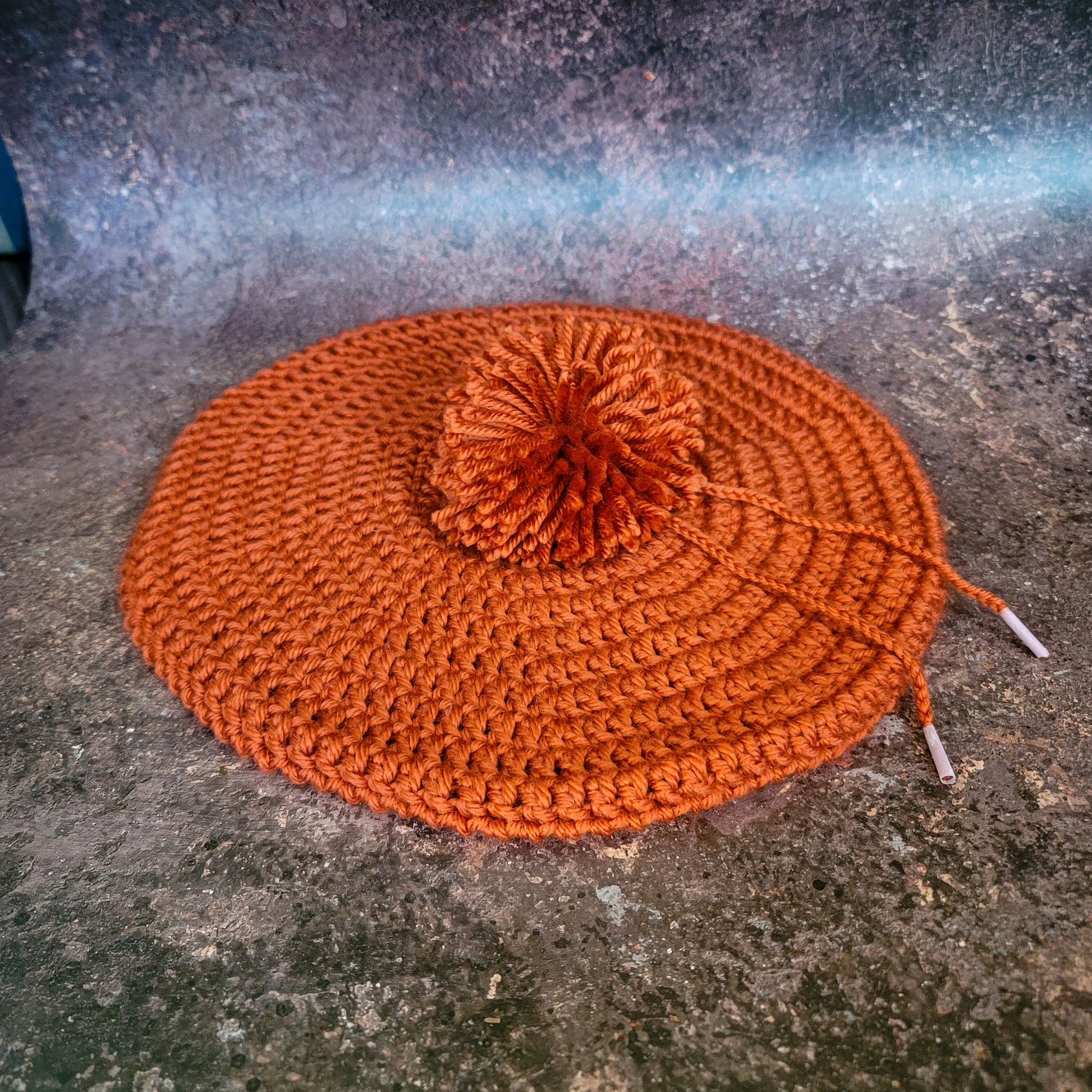 Rusty orange crocheted beret with pom-pom, flat lay.
