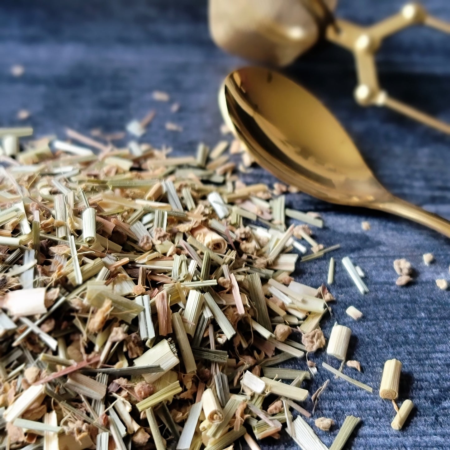 Loose organic lemongrass and ginger tea next to a spoon and tea strainer