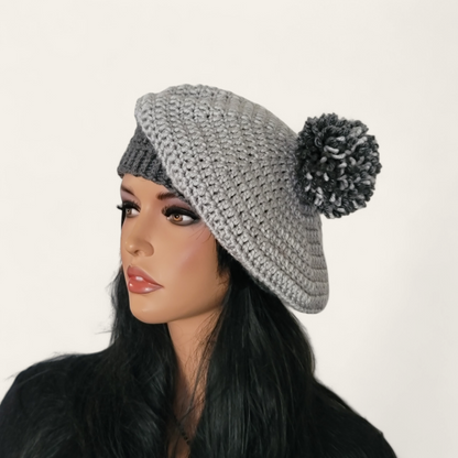 Two-toned grey crocheted beret with pom-pom on mannequin.