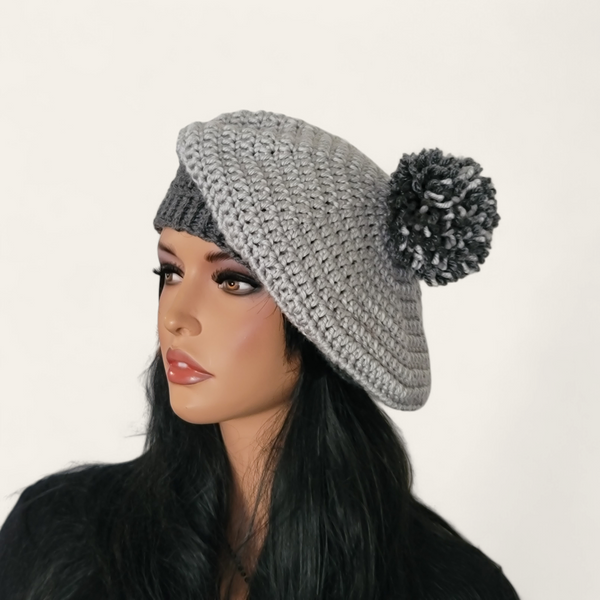 Two-toned grey crocheted beret with pom-pom on mannequin.