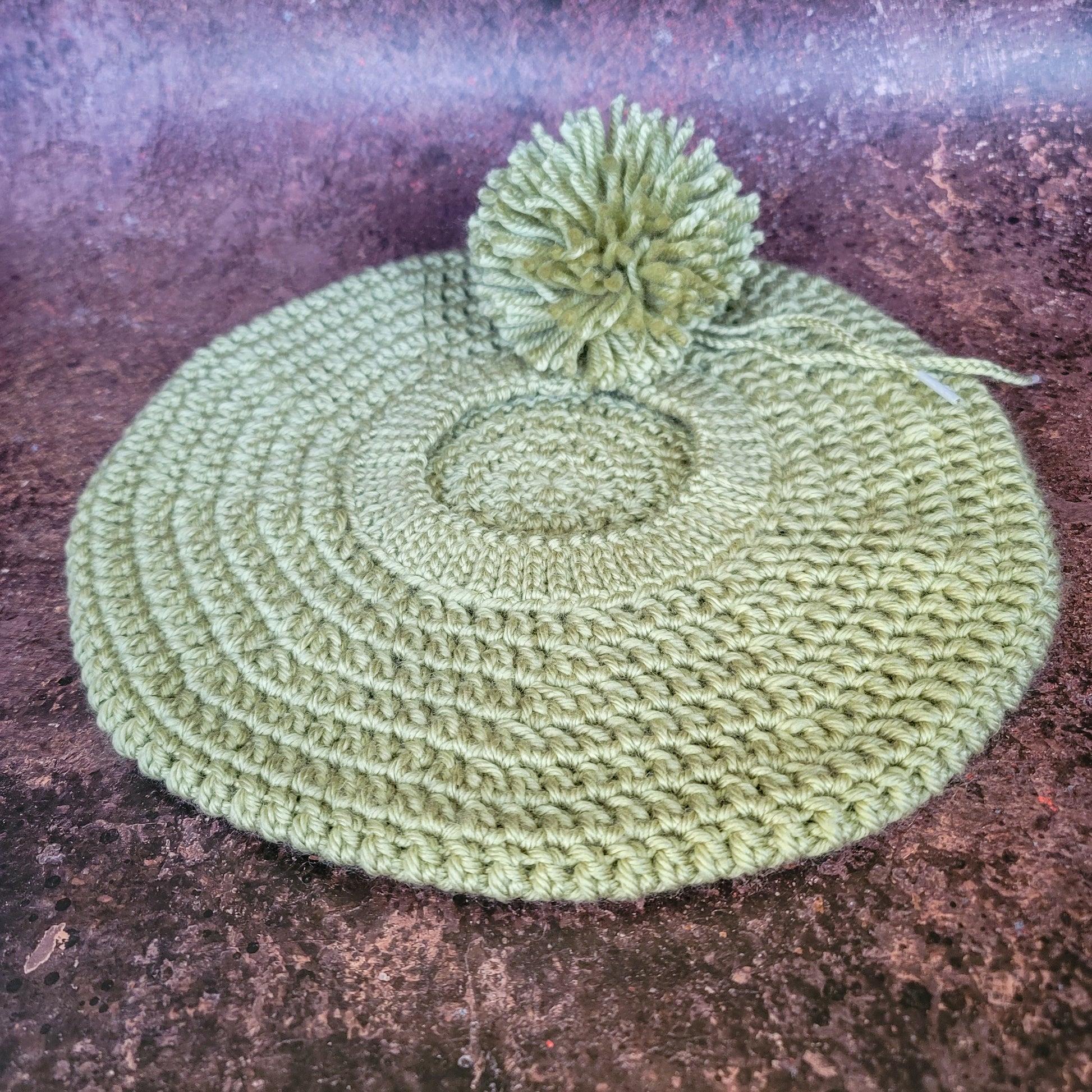 Flat Lay of celery green crocheted beret with detachable pom-pom on side