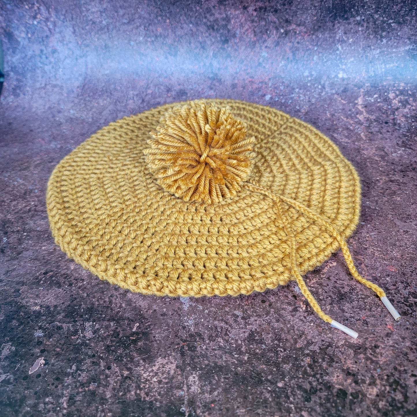 Gold crocheted beret with pom-pom, flat lay.