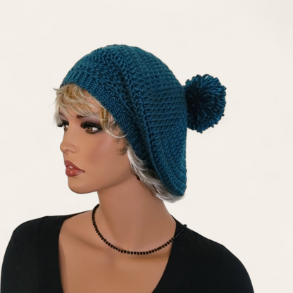 Teal crocheted beret with pom-pom on mannequin. 