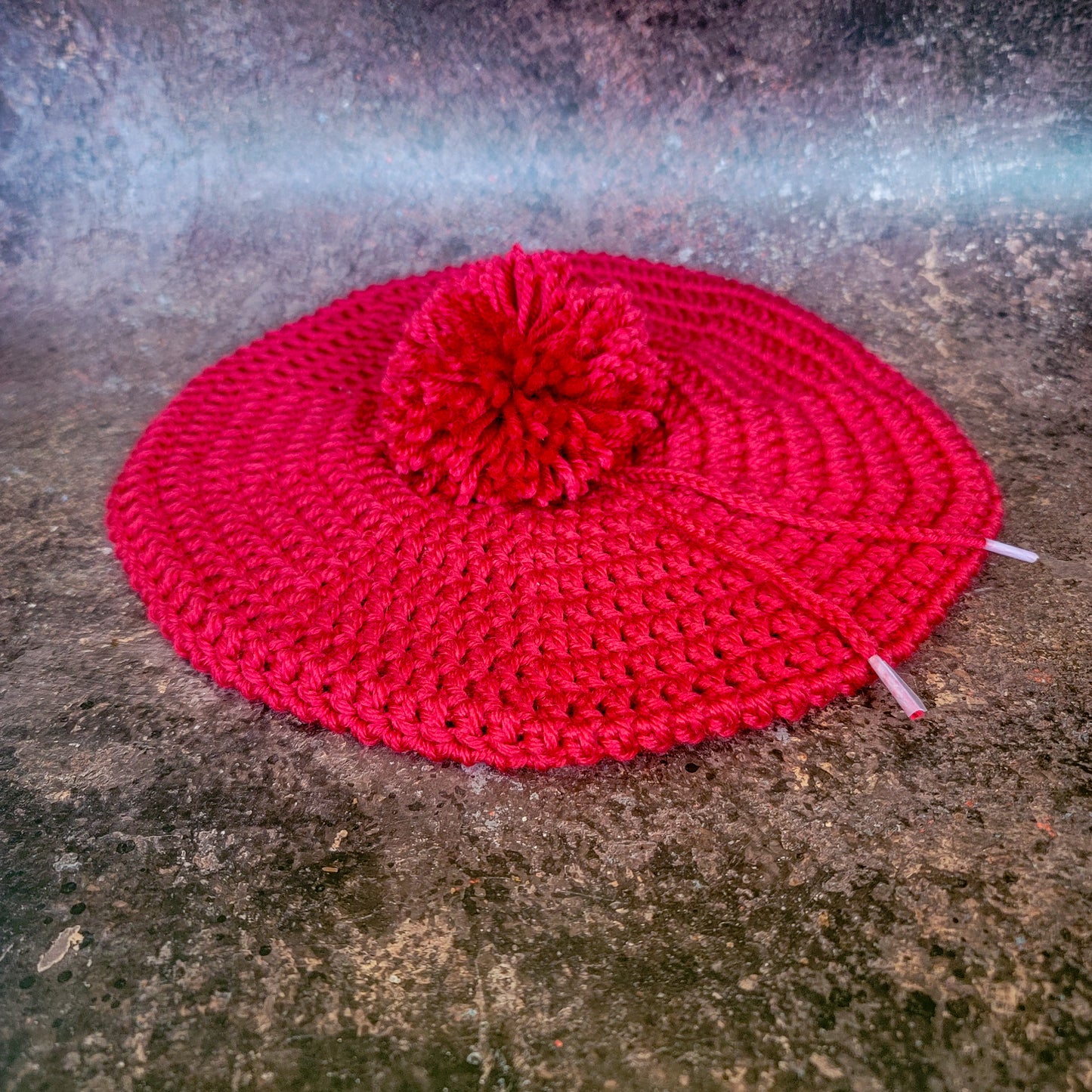 Red crocheted beret with pom-pom, flat lay.