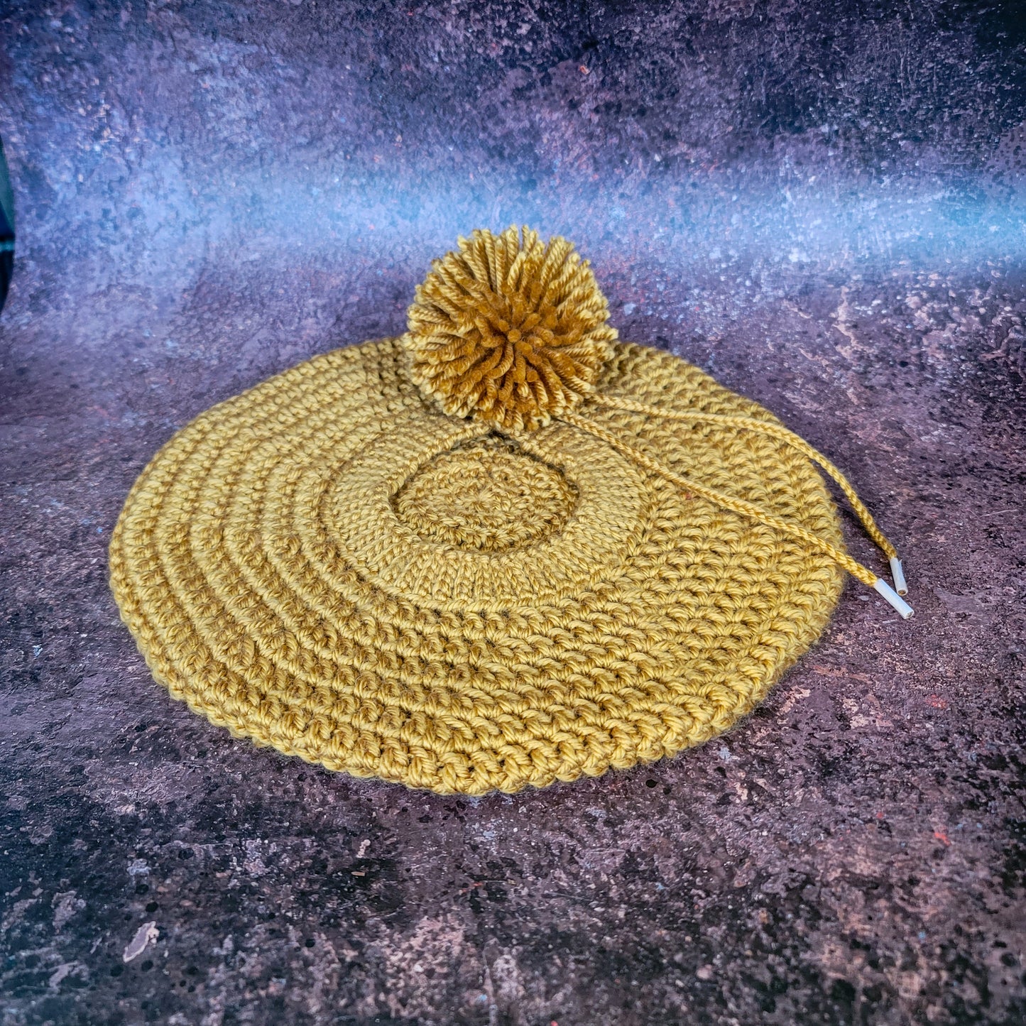 Gold crocheted beret with pom-pom on side, flat lay.