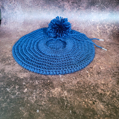 Indigo blue crocheted beret with pom-pom on side, flat lay.