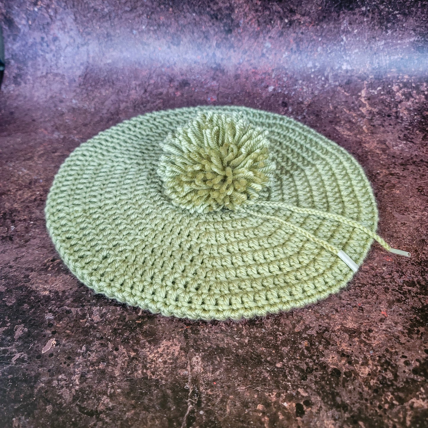 Flat Lay of celery green crocheted beret with detachable pom-pom.