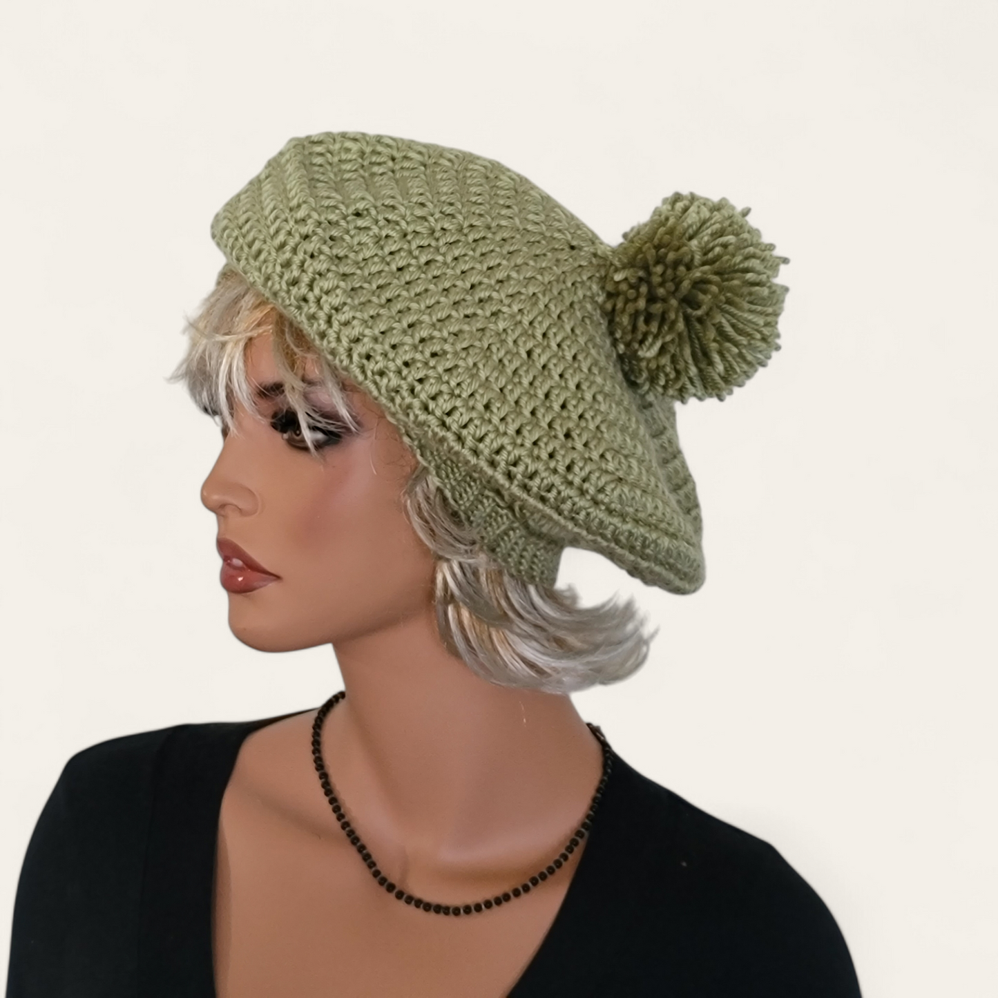 Celery green crocheted beret with pom-pom on mannequin.