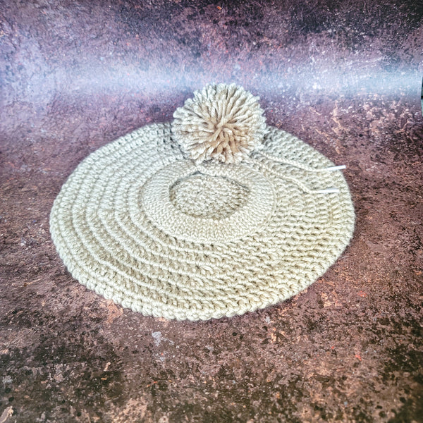 Tan crocheted beret with pom-pom on side, flat lay.