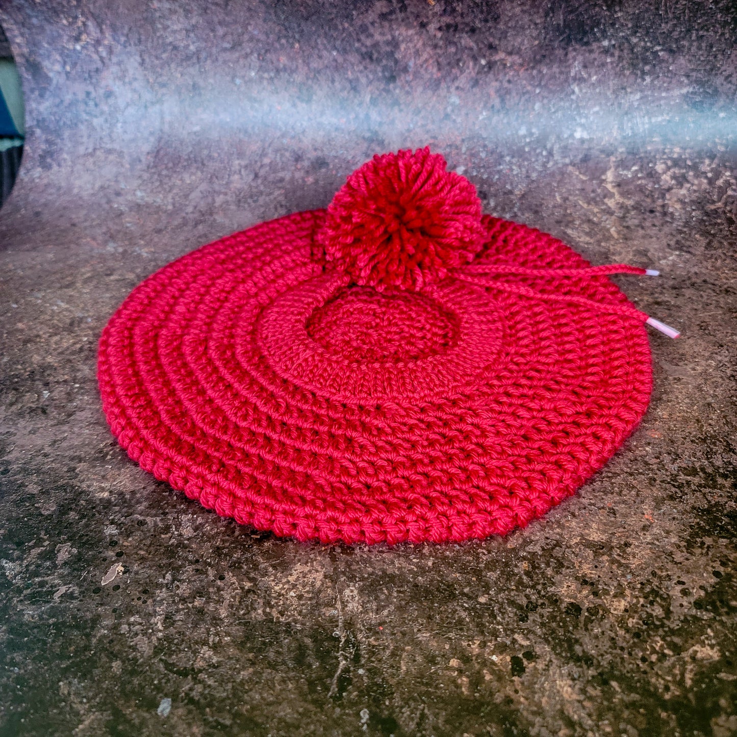 Red crocheted beret with pom-pom on side, flat lay.