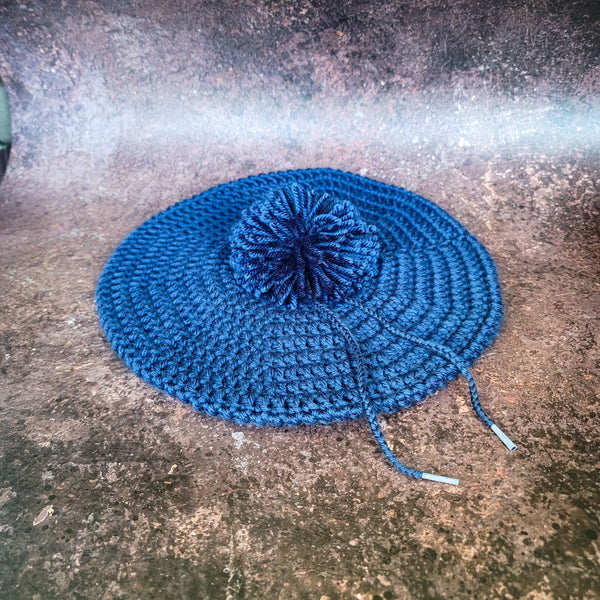 Indigo blue crocheted beret with pom-pom, flat lay.